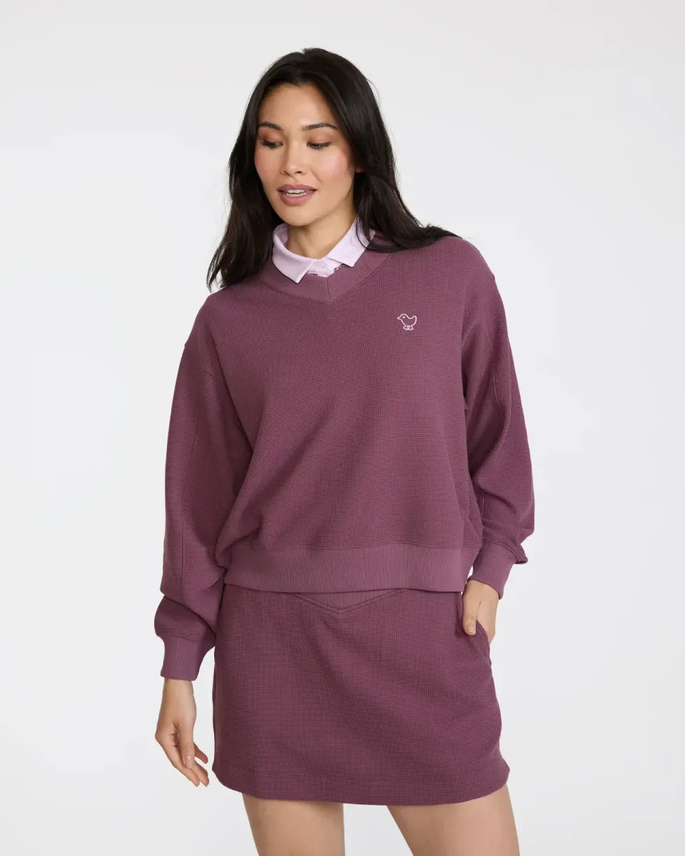Woman in a plum waffle V-neck over a pink polo with a matching skort