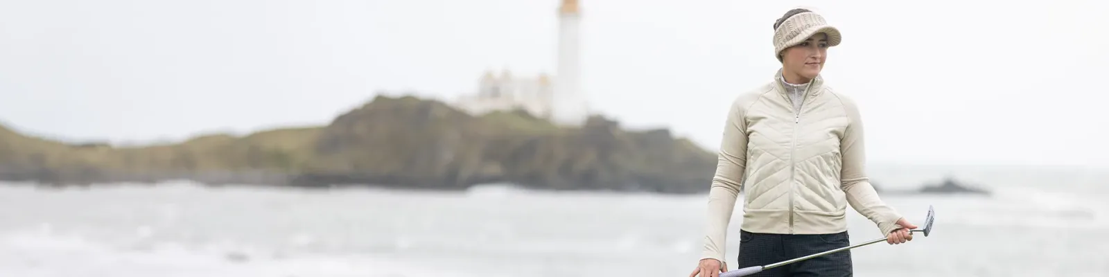 Woman golfer in a light jacket and visor on a links course by the sea